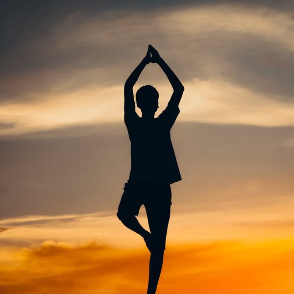 A person balancing on one leg in a serene natural environment at sunset.